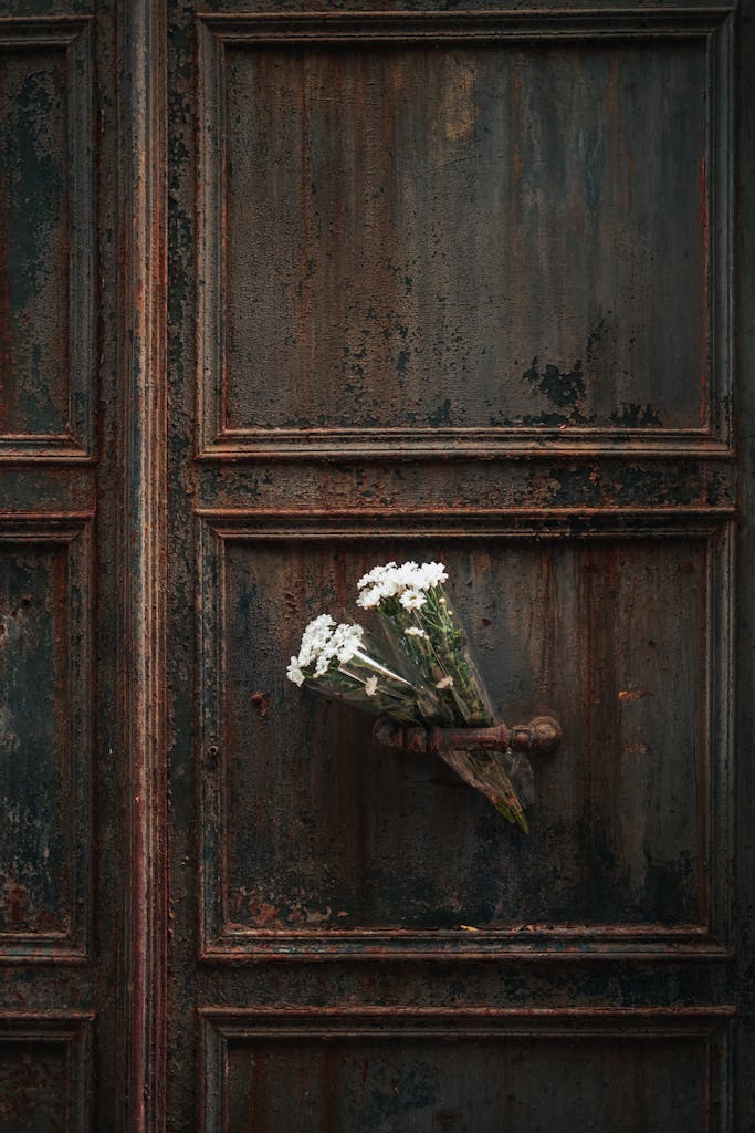 A rustic old door with a small bouquet of white flowers tucked in the handle.